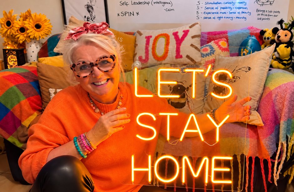 Jules at home in front of a neon sign that reads Let's Stay Home